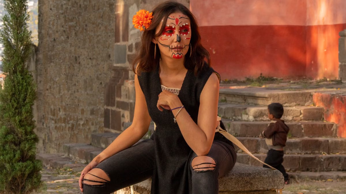 Woman in traditional Catrina makeup for Día de los Muertos with a vibrant orange flower.