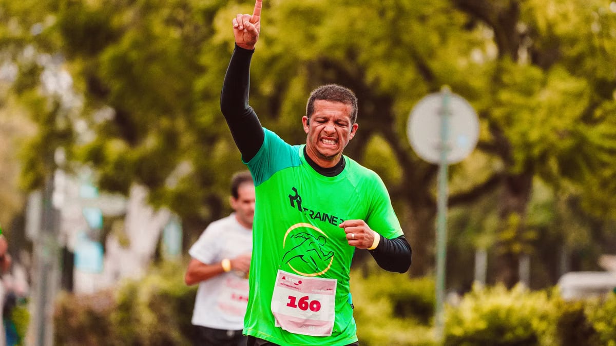 Joyful male runner celebrates a marathon win outdoors, raising arms in triumph.